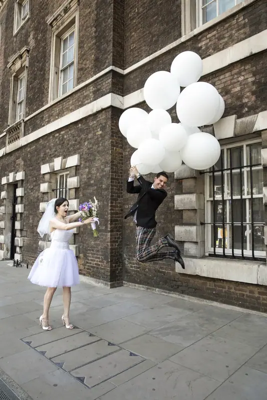 Bride and groom holding white balloons on a city street