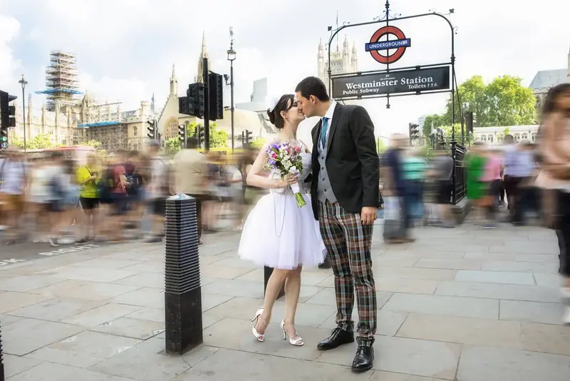 Bride and groom kissing beneath a London Underground sign on a busy street