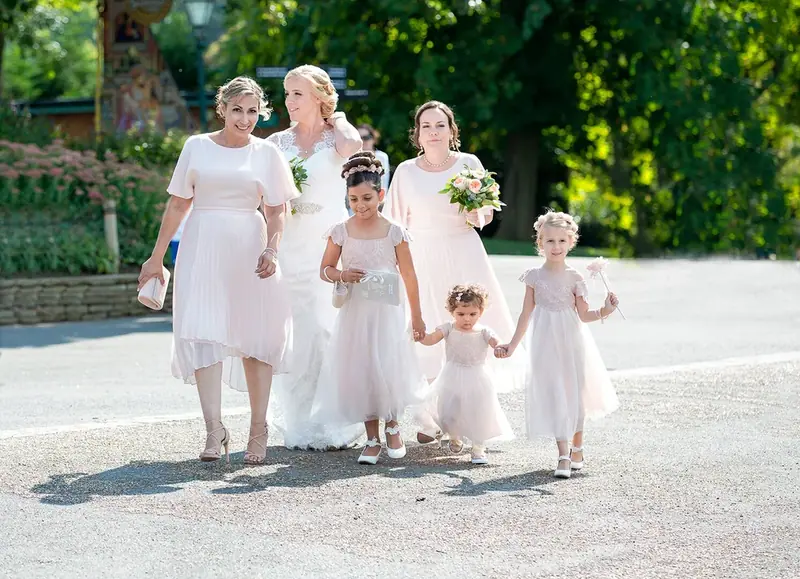 Bride with bridesmaids and flower girls in pale pink walking together in a park