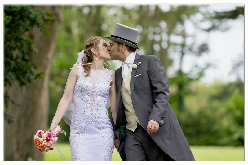 Bride and groom in a top hat kissing on a lawn