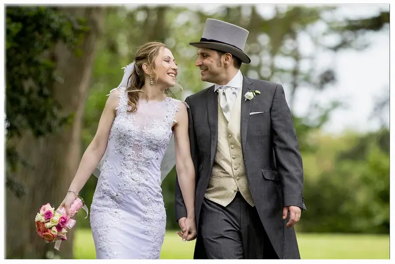 Bride and groom in a top hat walking hand in hand on a lawn