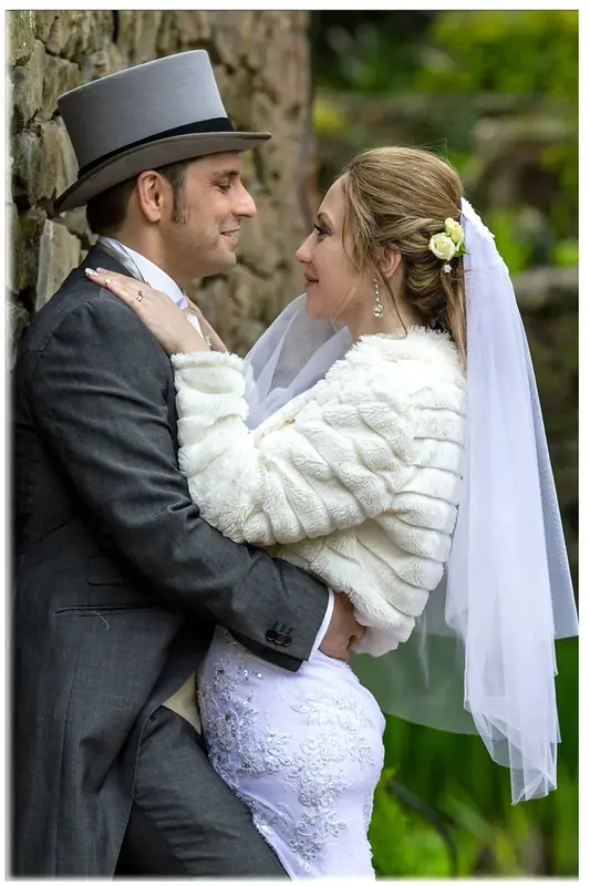 Bride in a fur stole and groom in a top hat embracing among trees