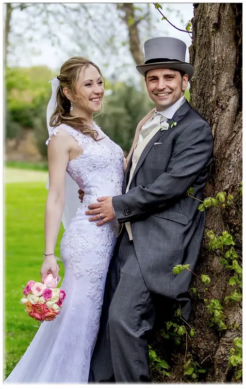 Bride and groom in a top hat embracing beside a tree