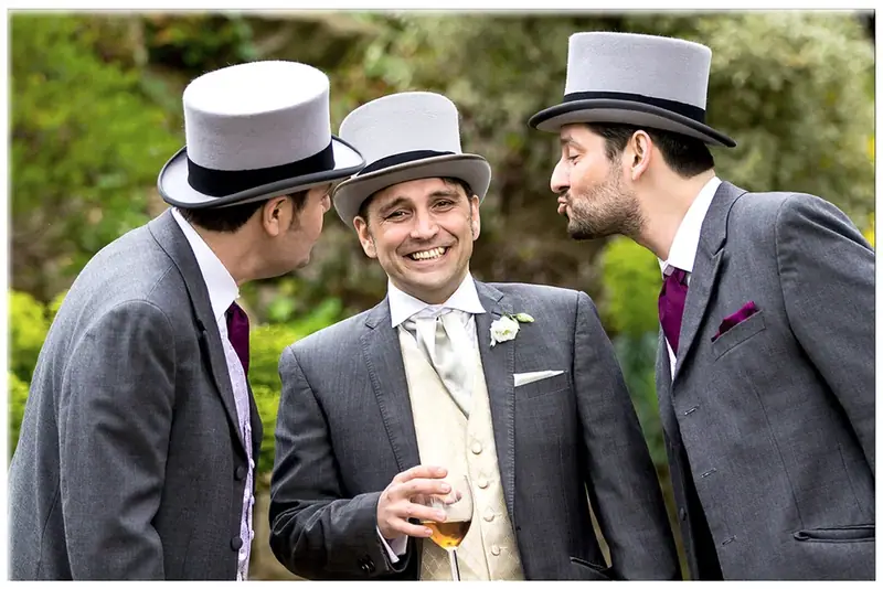 Groom and groomsmen in grey morning suits and top hats laughing together