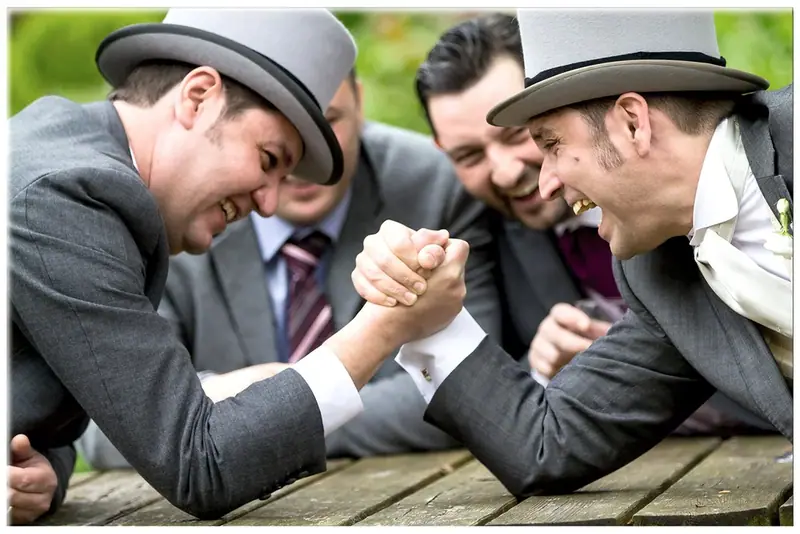 Groomsmen in top hats gathered around a table joking with the groom
