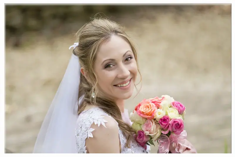 Smiling bride holding a pink and yellow bouquet beside a stone wall