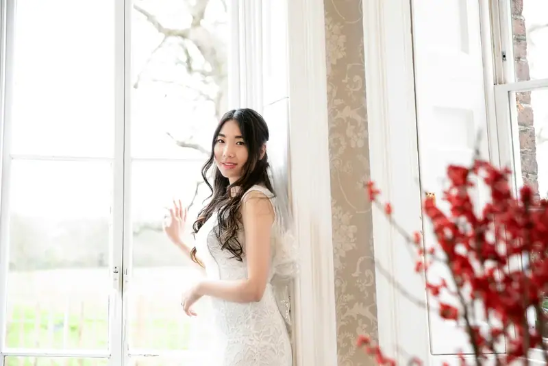 Bride standing by a window in a bright room with red blossom branches