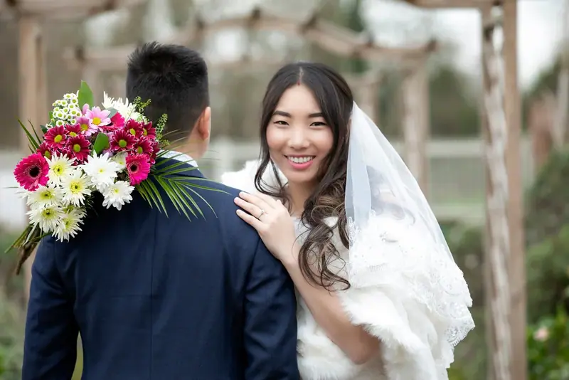 Bride in a fur wrap smiling at the groom, holding a colourful bouquet