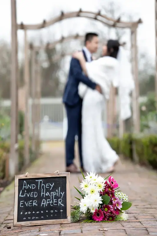 Bride and groom kissing beneath a pergola with a chalkboard sign and flowers