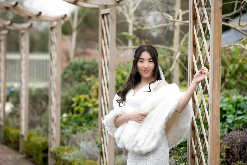 Bride in a fur wrap standing beneath a wooden pergola