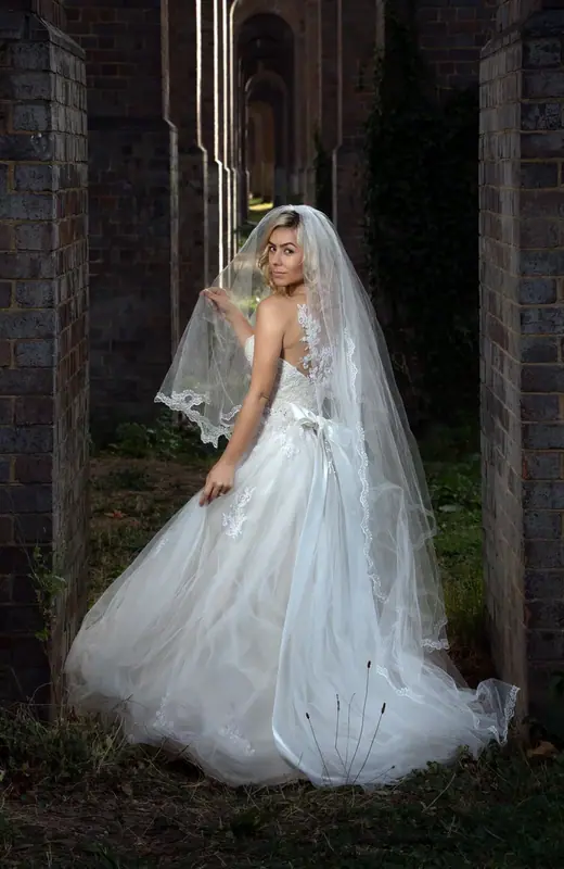 Bride in a long white gown and veil standing beneath old brick arches