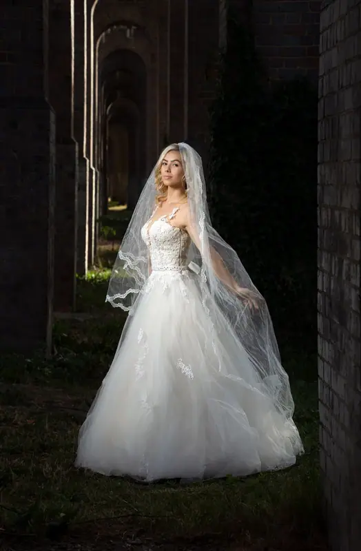 Bride in a white gown and veil framed by a brick arch