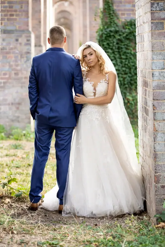 Bride and groom in a blue suit standing together beneath brick arches