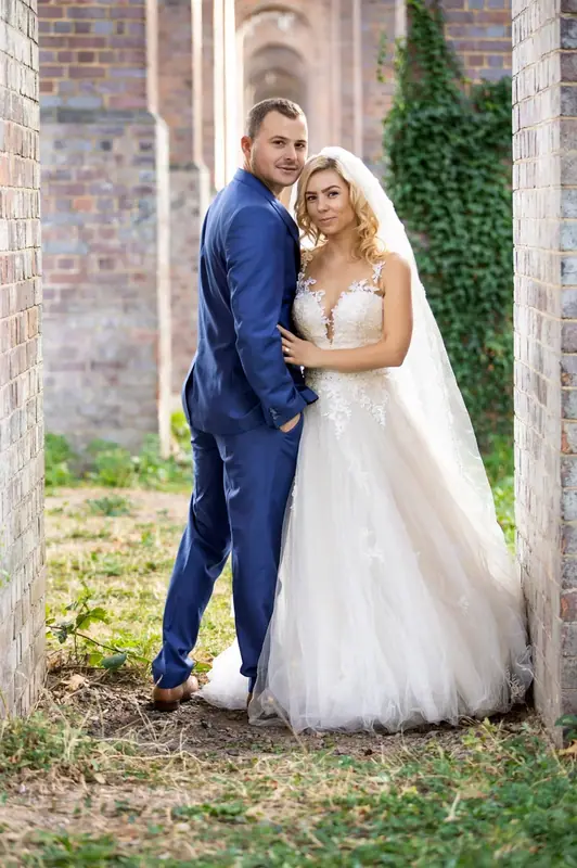 Bride and groom in a blue suit embracing in a brick archway