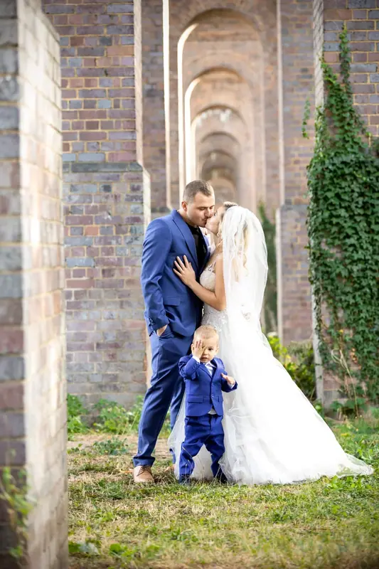 Bride and groom with a small boy beneath a row of brick arches