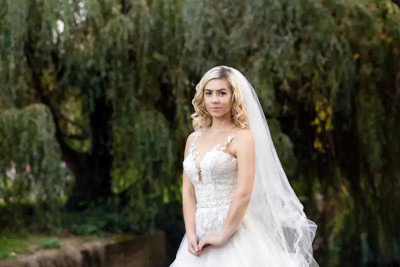 Bride standing beneath a willow tree beside a river