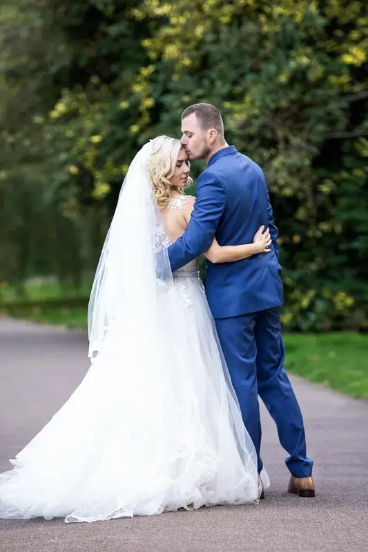 Bride and groom embracing on a path beneath trees