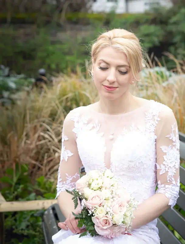 Bride in a lace gown holding a bouquet, seated among tall grasses