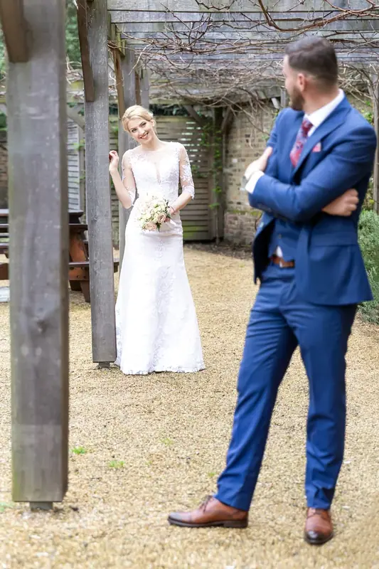Bride and groom in a blue suit standing under a pergola