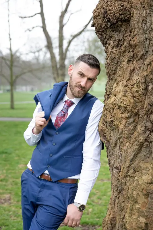 Groom in a blue waistcoat leaning against a tree